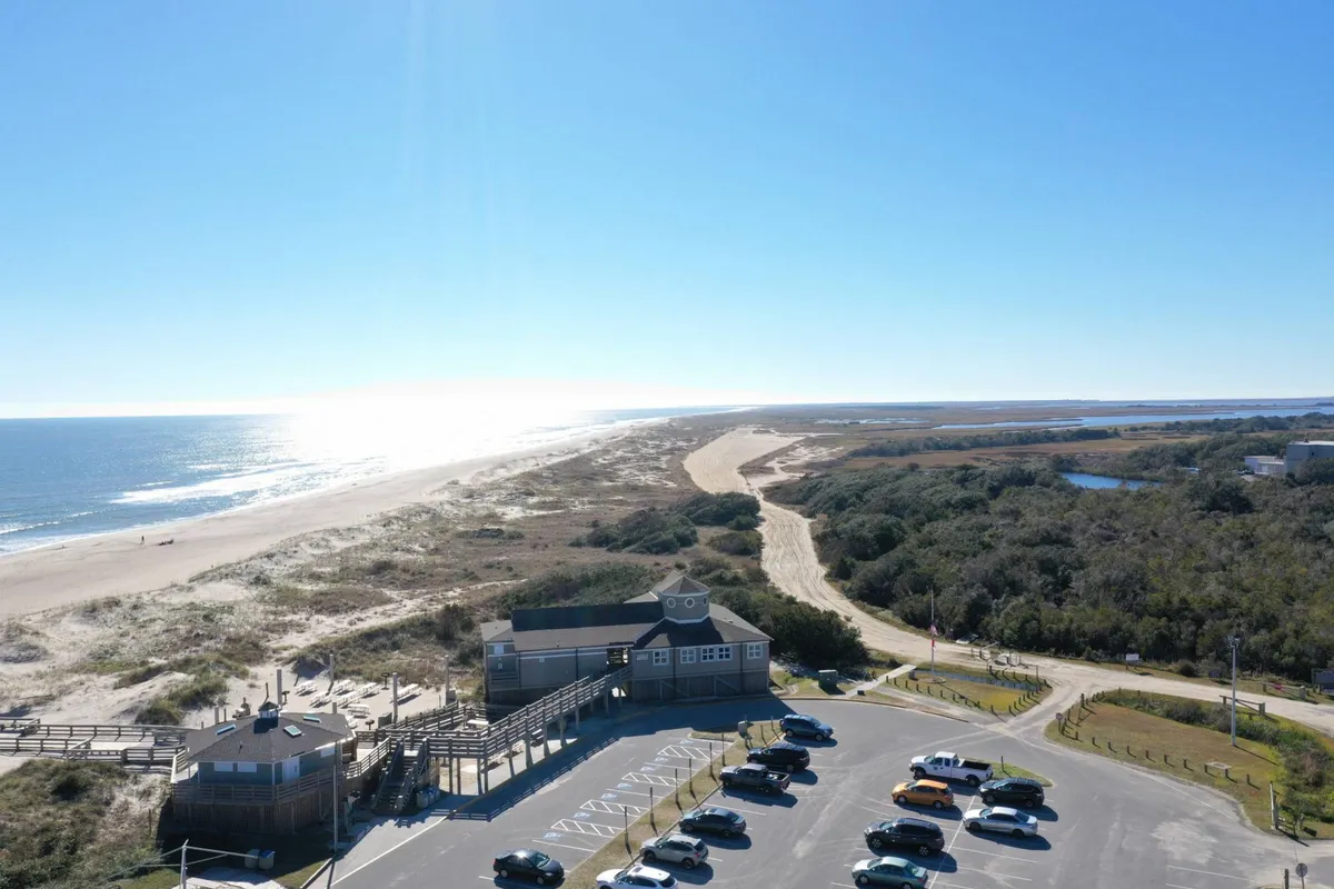 A wide exterior shot capturing the parking area with the beach, ocean, walking paths, and the condo building visible. This image situates the property in its broader context, showing the dedicated parking and the easy access to both the building and the sand.