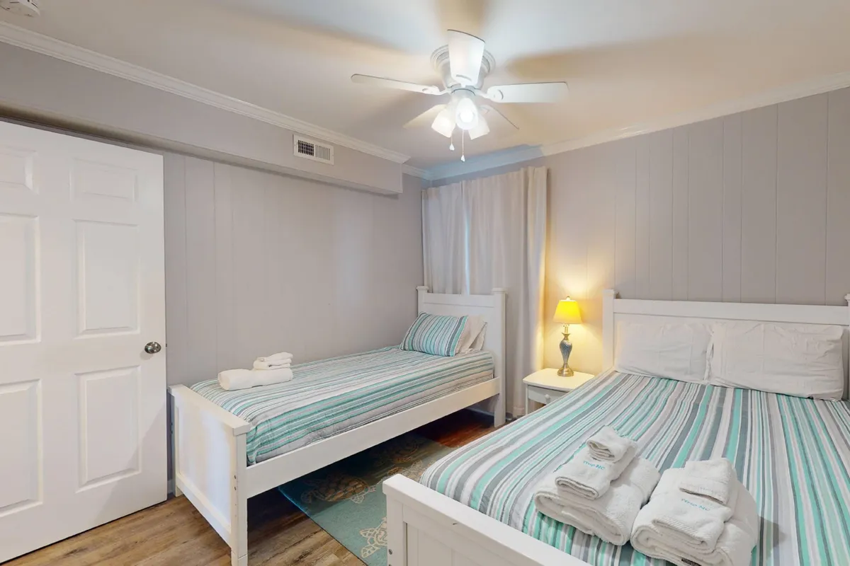 This bedroom offers two twin beds with striped bedding, a bedside lamp, and a window with soft curtains letting in sunlight. The ambiance is cozy and inviting, making it a suitable retreat for kids or friends to relax and unwind after a day of adventure.