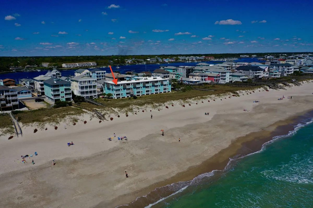 A cheerful, inviting view of a beachfront property with soft sand dunes and the blue ocean stretching into the distance. Children and families can be envisioned building sandcastles or playing at the water’s edge, with the home offering a clear connection to the lively beach scene.