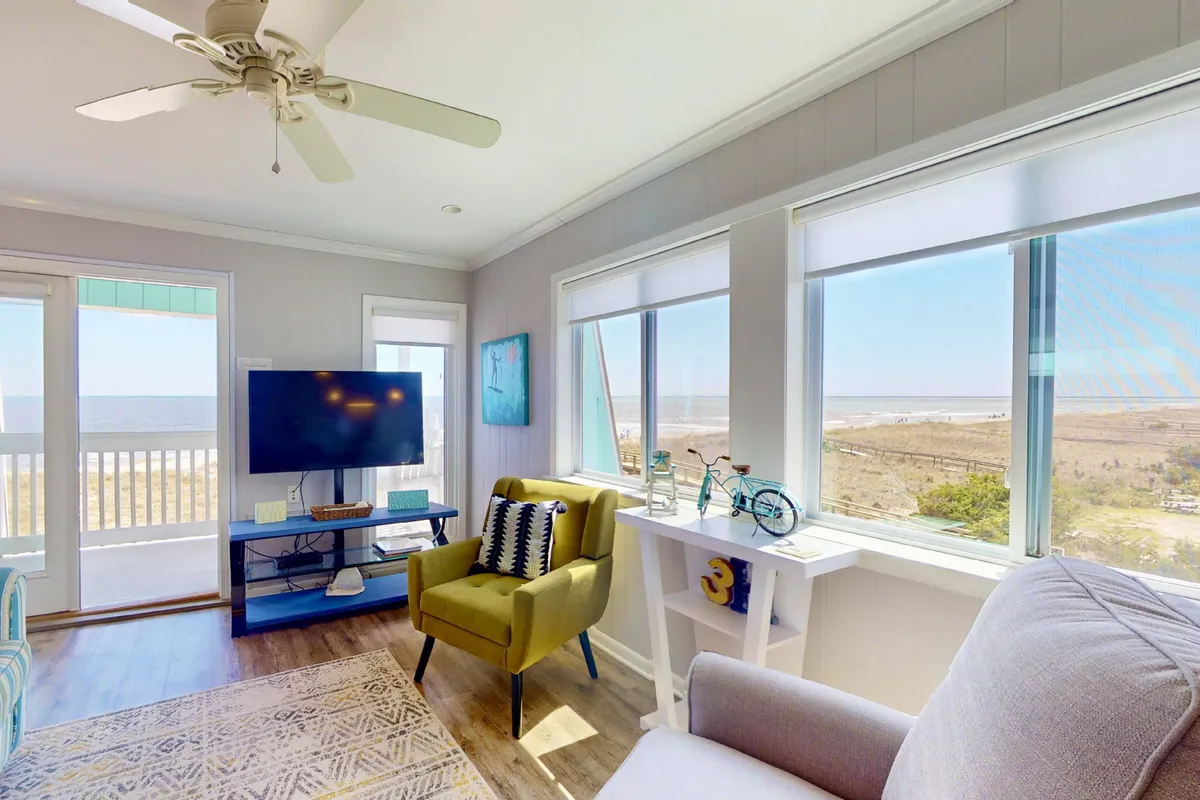 A bright, cheerful interior with a large window showcasing an expansive ocean view. A comfortable green chair is positioned to take in the scenery, and the space is filled with natural light, creating an uplifting environment for work or relaxation.