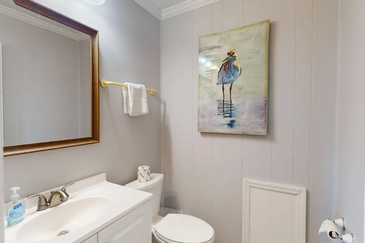 A bathroom vanity with a sink, a framed mirror, and artwork of a bird creates a fresh and inviting space. The area is well-lit and organized, perfect for personal grooming and unwinding after a long day in the sun.