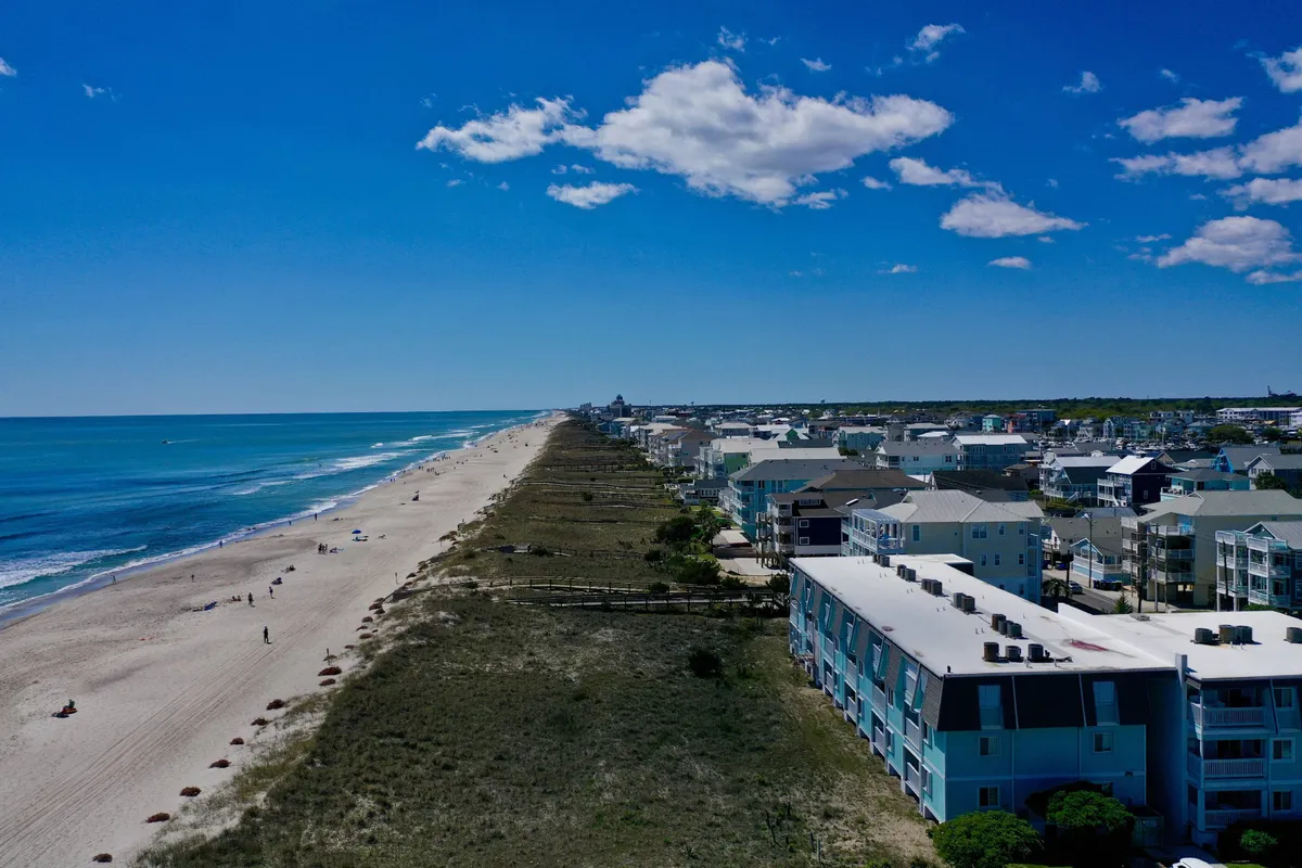 A sweeping view of the beach, ocean waves, and a row of colorful beach houses lining the shore. The scene is vibrant, with people enjoying the sand and water, and the atmosphere feels relaxed and inviting—perfect for group activities and water sports.