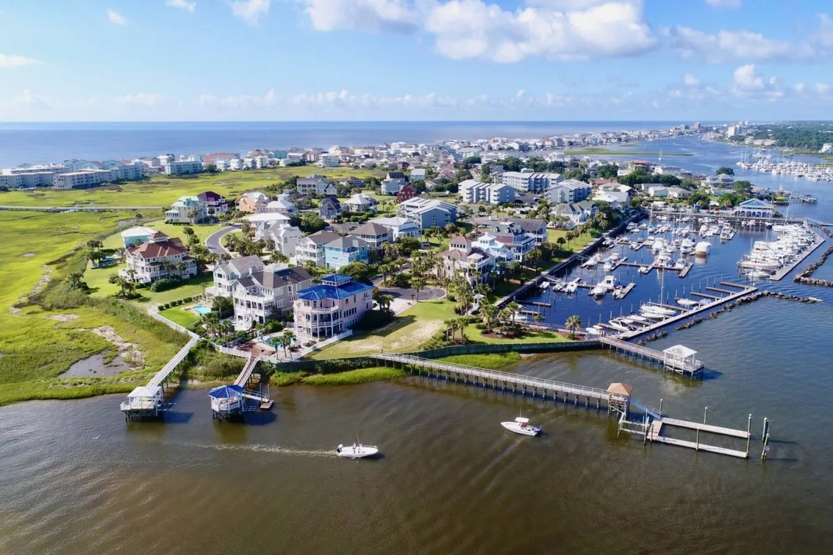 A serene marina scene with boats docked alongside vibrant houses and grassy areas leading to wide waterways. The calm water reflects the sky at sunset, providing an inviting option for a dinner cruise or peaceful evening by the marina.